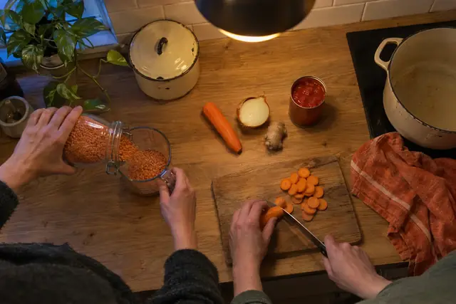Hände füllen rote Linsen in einen Messbecher, daneben Möhre, Zwiebel, Ingwer und eine Dose Tomaten.