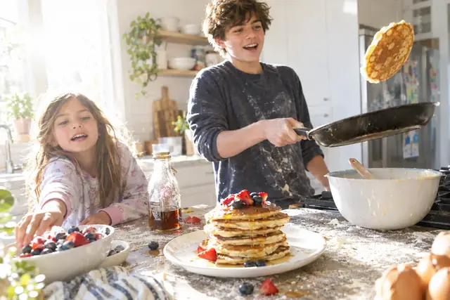 Ein Jugendlicher wirft Pfannkuchen in der Küche, seine jüngere Schwester greift nach den Beeren.